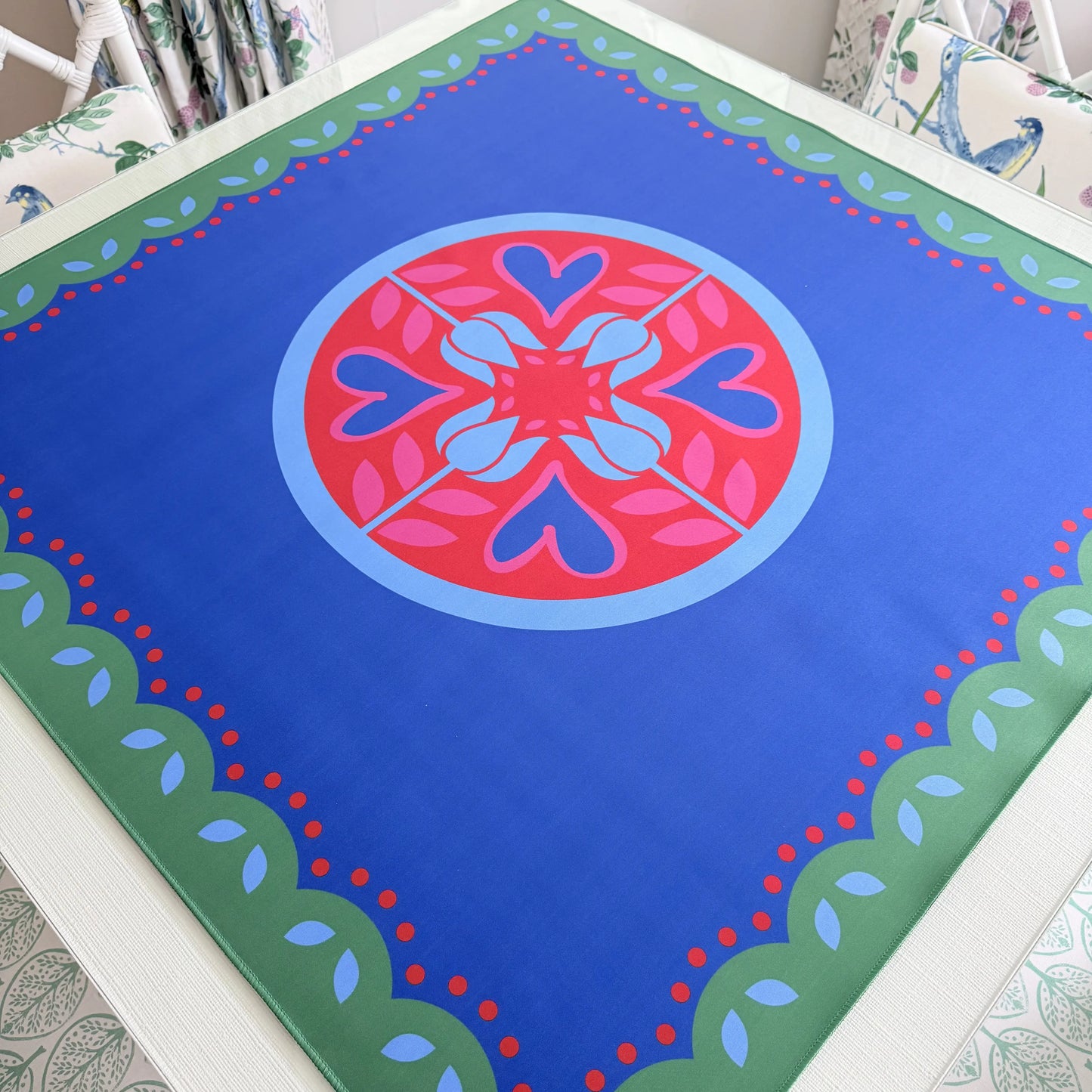 Photograph of a luxury Hearts & Flowers mahjong mat featuring vivid azure and red tones with soft gray green details and subtle pink accents in a festive floral and holiday-inspired design.