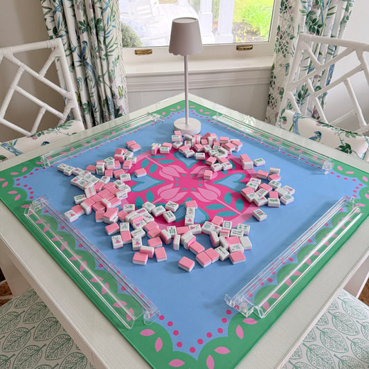 Photograph of the Hearts & Flowers Pastel Garden mahjong mat featuring floral and heart-inspired artwork in pastel azure, green, vivid magenta, light magenta, and cyan tones, styled with cabana pink mahjong tiles, transparent clear racks, and a cordless white LED lamp.