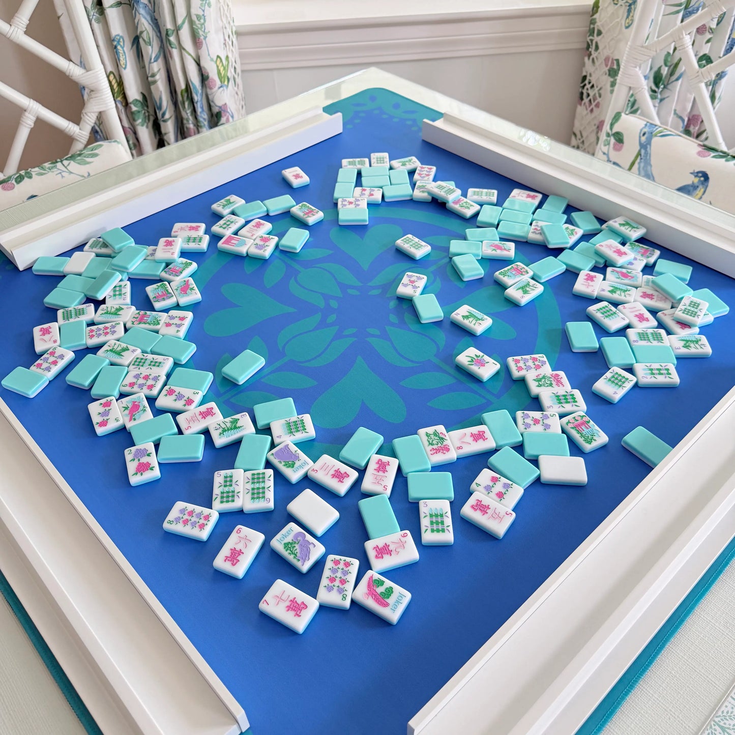 Photograph of the Hearts & Flowers Azure Bloom mahjong mat styled with white wooden mahjong racks and Southern Springs mahjong tiles spread across the playing surface.