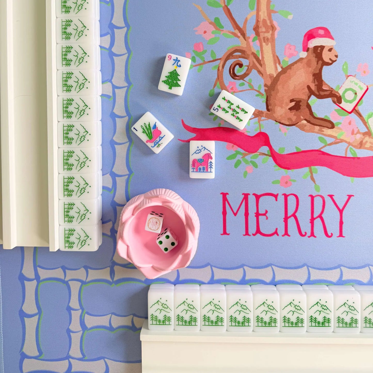 Closeup of the bamboo blossom Christmas mahjong mat, showcasing a monkey with a Christmas hat, resting on bamboo. Displayed with dice, white wooden racks and Christmas tiles.