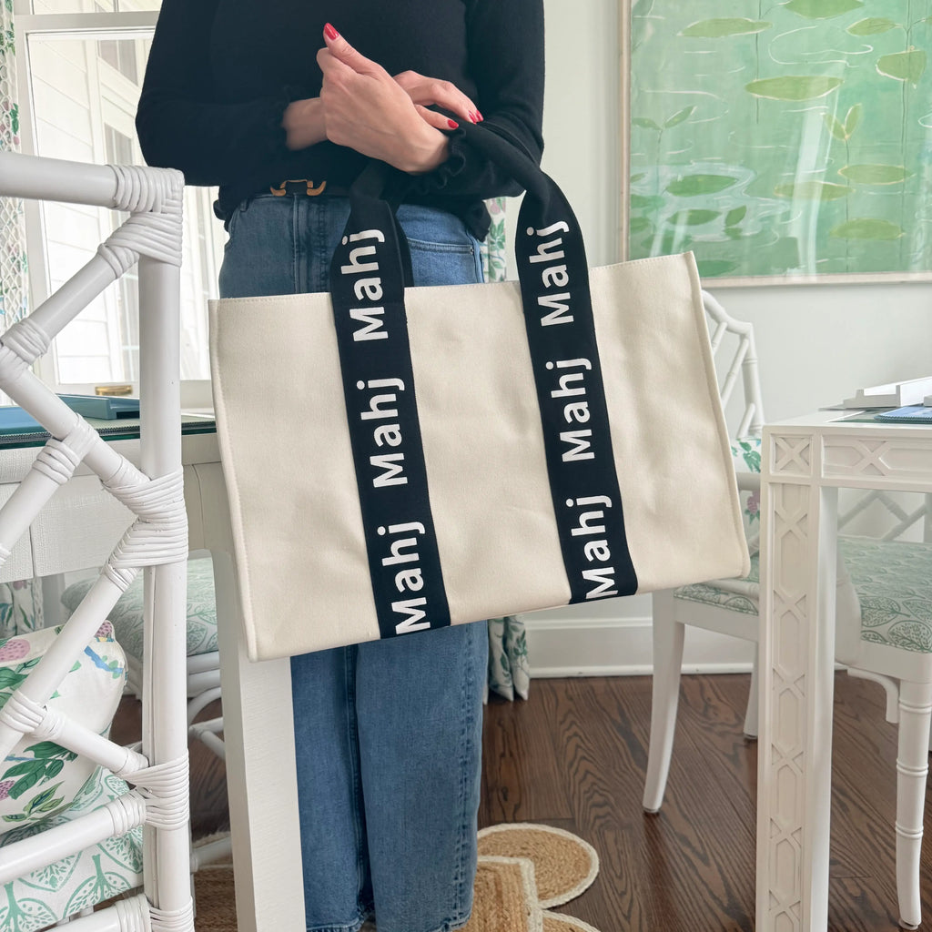 Person carrying a black oversized Mahjong tote bag by the handles to showcase its size and structured design.