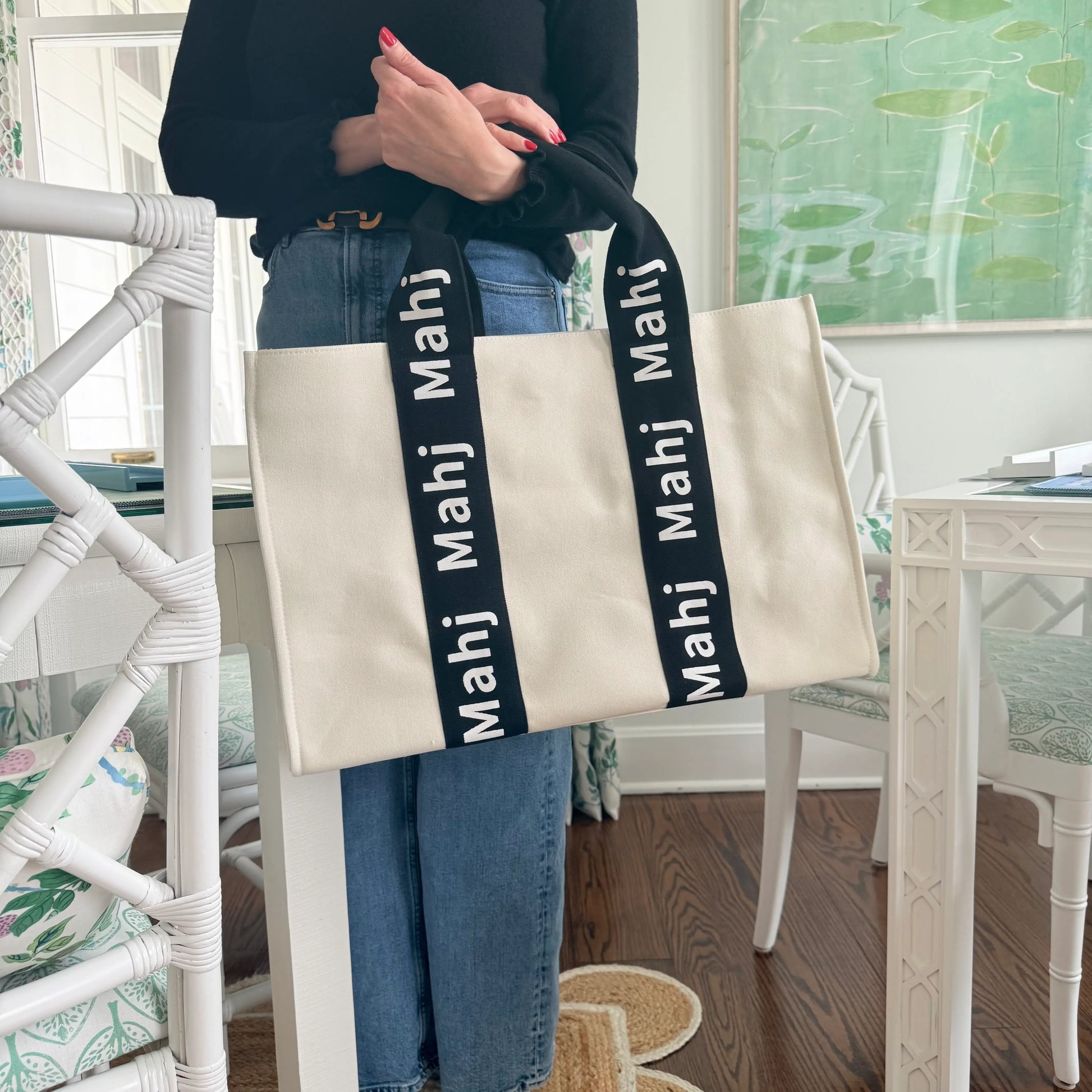 Person carrying a black oversized Mahjong tote bag by the handles to showcase its size and structured design.