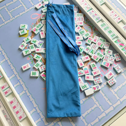 Blue velvet mahjong rack bag showcasing its themerrymahjongco ribbons, resting on the blue Bamboo Blossom Mahjong Mat with the Southern Springs Tile set and White Wooden Racks.
