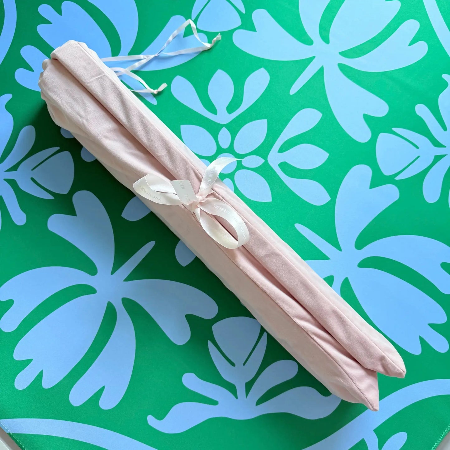 Dusty light pink velvet mahjong rack bag help together with a bowtie, resting on the Emerald Mist Mahjong Mat from the Tulip Terrace Mat Collection.