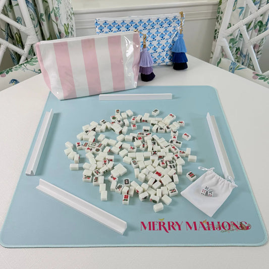 Mini Mahjong travel set in play with miniature tiles, white racks, pink striped tile bag, blue blockprint bag, and light blue travel mat.