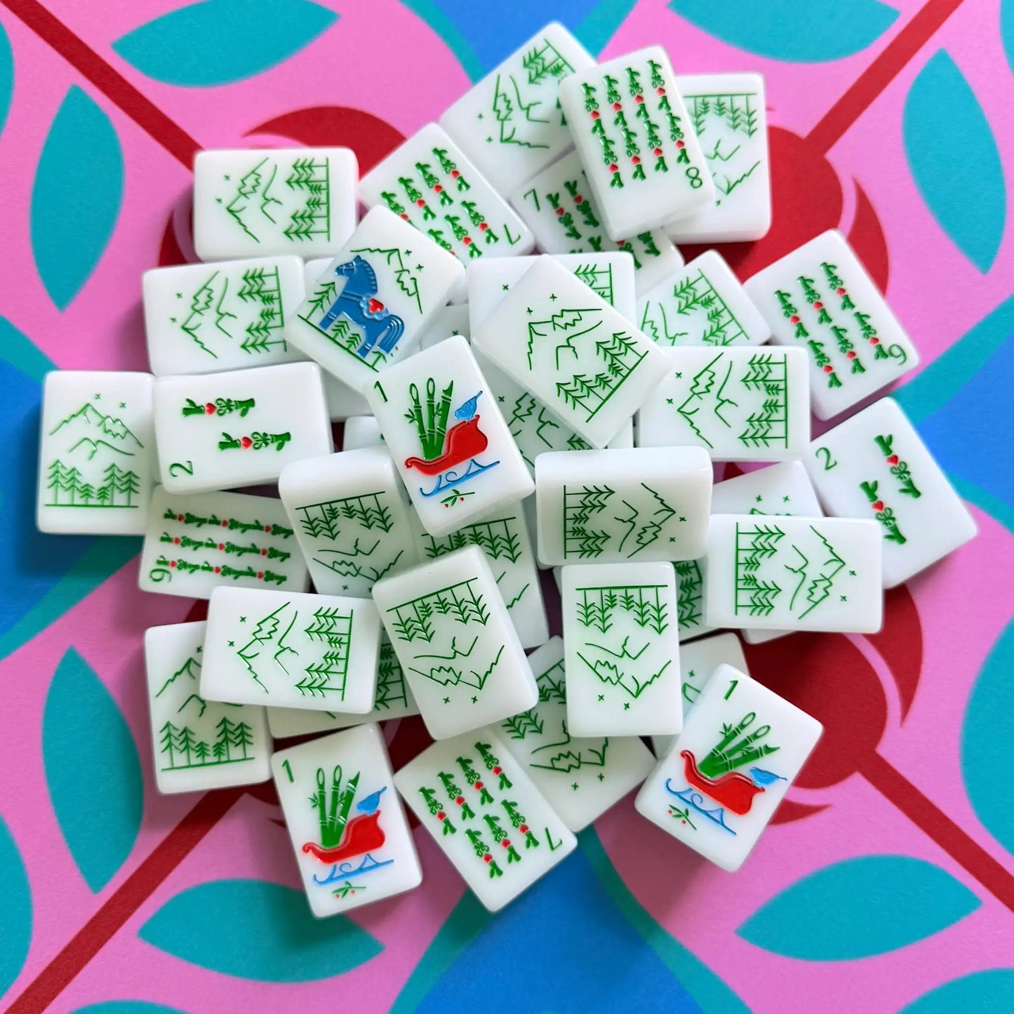 A pile of The Scandinavian Christmas Red & Green Mahjong Tile collection's bam tiles showcased on top of the Peppermint Bloom Mahjong Mat.
