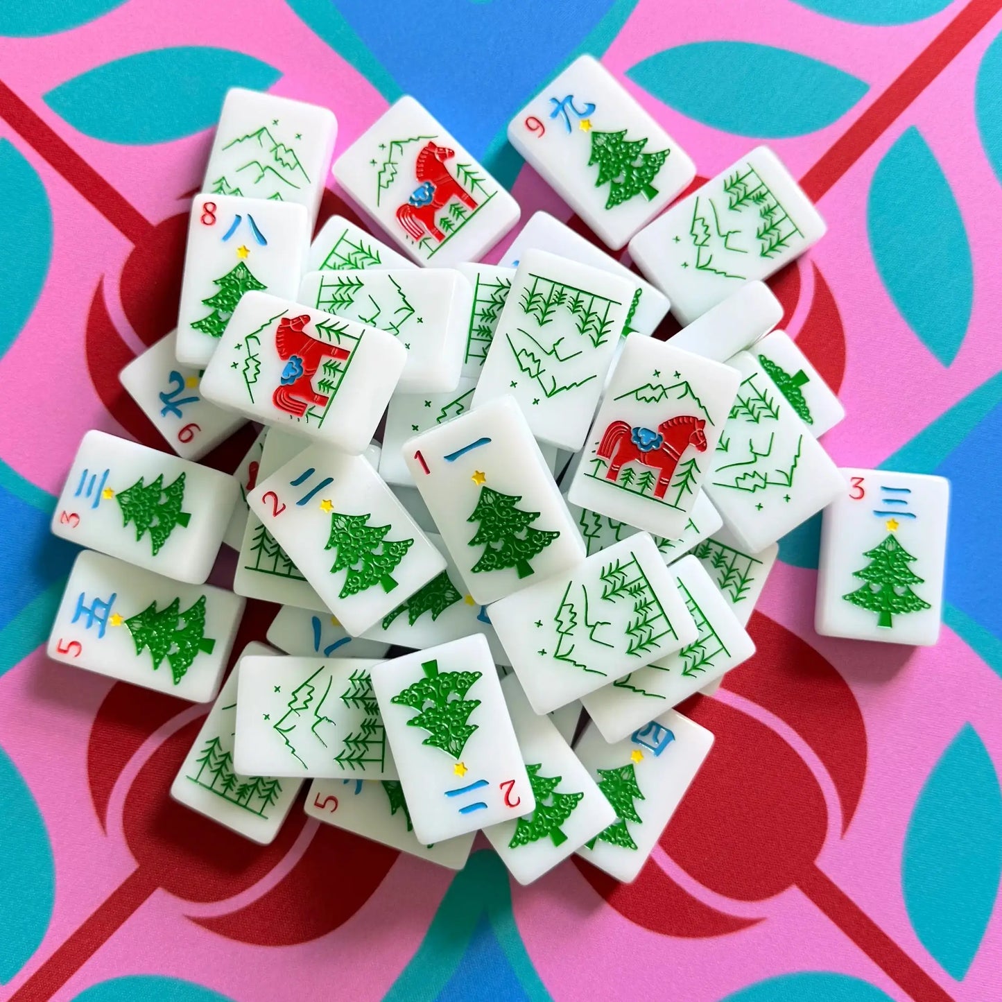 A pile of The Scandinavian Christmas Red & Green Mahjong Tile collection's crack tiles showcased on top of the Peppermint Bloom Mahjong Mat.
