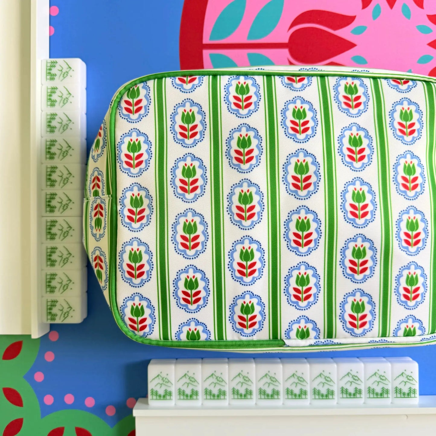 A showcase of the Scandinavian Christmas Red & Green Mahjong Tile collection with the backs of the tiles highlighted resting against white wooden racks with a matching bag on the Peppermint Bloom Mahjong Mat.
